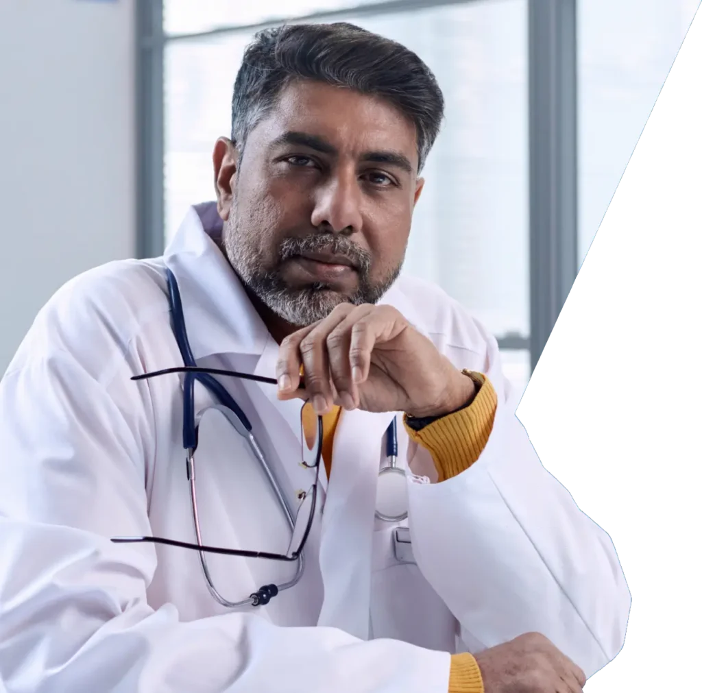 A male doctor wearing a white coat and glasses, standing confidently in a clinical setting.